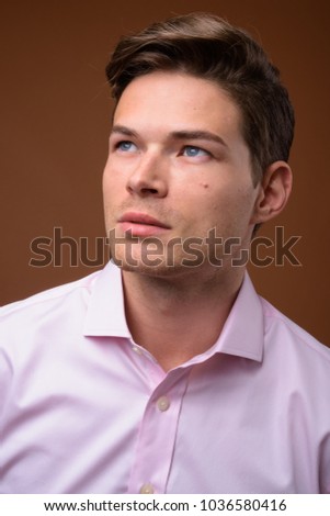 Studio shot of young handsome businessman wearing pink shirt against brown background