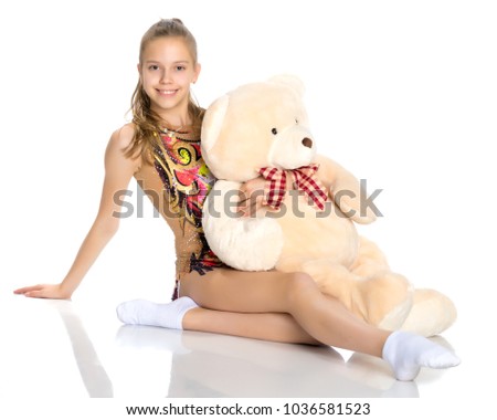 A girl gymnast sits on the floor with a teddy bear. The concept of sport, fitness, happy childhood. Isolated on white background.