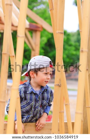 Curious child wearing reversed cap has fun in asian playground landscape, behind the bamboo sticks. Cute boy playing in public park with asian exotic installations. Beautiful and happy 3 year old kid.