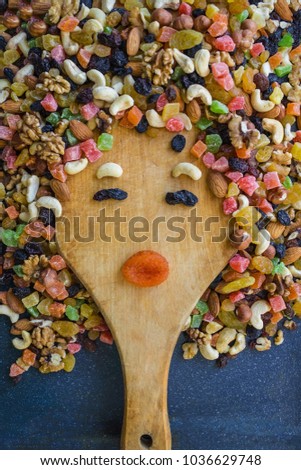 Cashew, dried apricots, raisins, almonds, candied fruits, walnuts are mixed and laid out on a cutting board in the form of a woman's face. View from above.