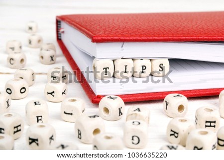 Word Tips written in wooden blocks in red notebook on white wooden table. Wooden abc.
