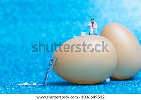 Miniature people :Painter is painting Easter-eggs for Easter day on blue glitter  background