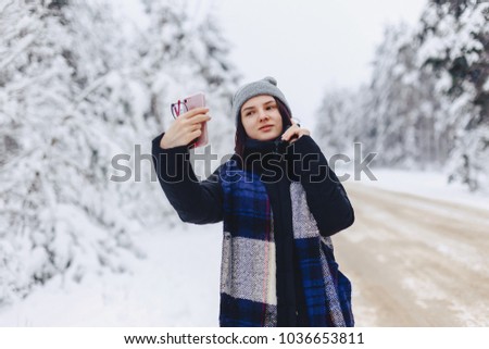 A pretty girl makes a selfie in the middle of a snowy forest road in winter