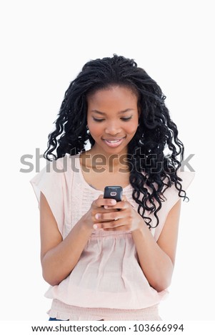 A smiling girl is texting on her mobile phone against a white background