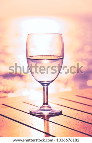 Silhouette glass of wine on a wooden table with  seascape and skyline in the evening with sunset tone style.