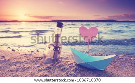 romantic sunset at the beach with bottle with a message and paper boat