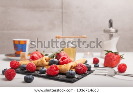 Pancake dish with fresh fruits strawberry blueberry and raspberry on a white wooden table. On the side coffee and honey and sugar.