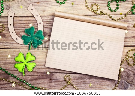 Blank notepad with horseshoe and felt clover leaves on wooden boards. St.Patrick's day holiday symbol. Space for text.