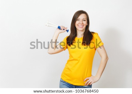 Beautiful European young happy brown-haired woman holding, blowing in football pipe, dressed in casual clothes, yellow t-shirt with shy charming smile isolated on white background. Sport fan concept