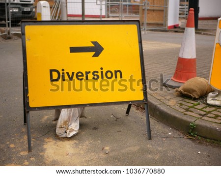 Yellow and black British diversion sign with arrow pointing right and traffic cone in urban environment