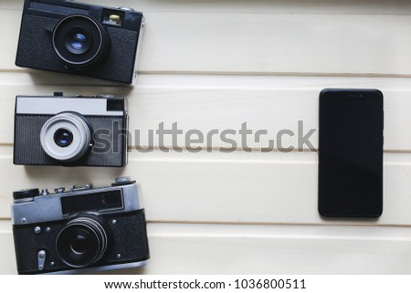 Old photo cameras and black smartphone on wooden texture. Vintage film camera with on beige background. Retro and antique photography.