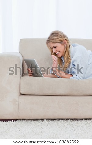 A woman who is lying on a couch is holding a tablet and laughing