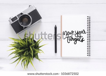 Minimal Workspace - Flat lay view photo of working desk with new year target calligraphy notebook and a camera lying on white wooden background. Top View flat lay photography. New year 2018 concept