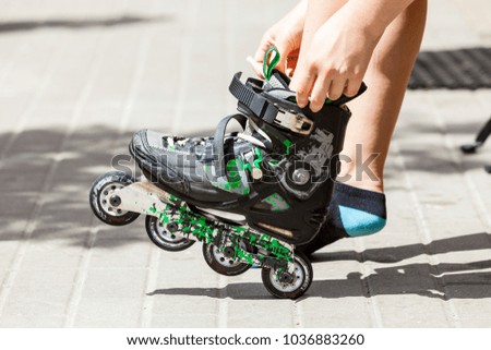 Happy joyful young woman putting on roller skates. Female being sporty having fun during summer in city