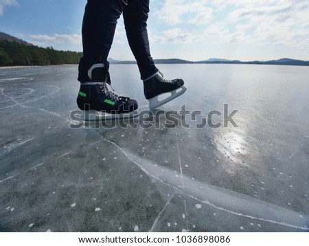Man ice skating on frozen lake. Thin ice with deeep cracks below man legs.