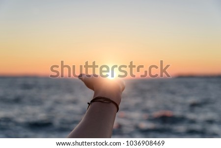 Female hand reaches for the sun at sunset against the background of the sea. Royalty-Free Stock Photo #1036908469