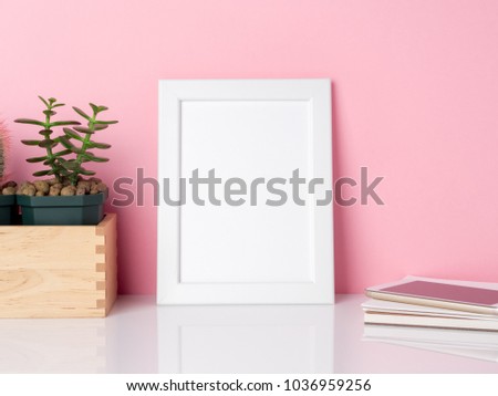 Blank white frame and plant cactus on a white table against the pink wall with copy space. Mockup with copy space.