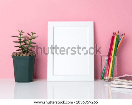 Blank white frame, crayon in jar, plant cactus  on a white table against the pink wall with copy space