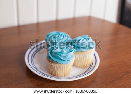 Trio of vanilla cupcakes with blue icing on a plate
