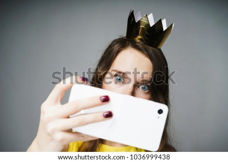 cute blue-eyed girl with a crown on her head makes selfie on her smartphone