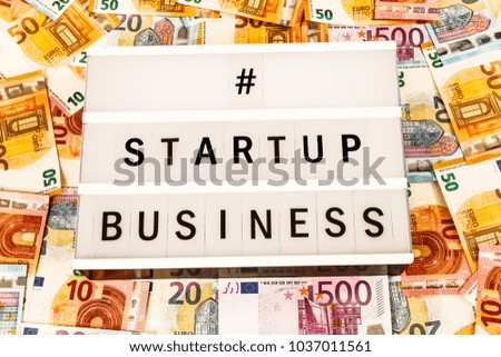 Text  Startup Business written on lightbox surrounded with Euro Banknotes