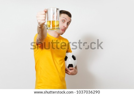 Inspired young fun European man, fan or player in yellow uniform hold in front face pint mug of beer, soccer ball cheer favorite football team isolated on white background. Sport, lifestyle concept