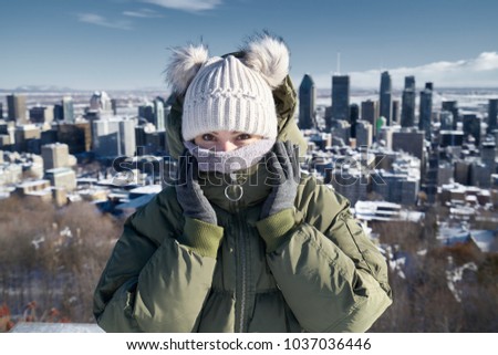 Cute girl in hat and warm coat in cold sunny windy day on Mount Royal, vith Montreal view on background