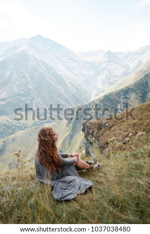 Beautiful young woman in a long dress sits on a background of mountains. Caucasus Mountains in Georgia