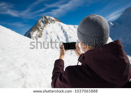 Mockup image of man hand holding black mobile phone with blank black screen on thigh in mountains