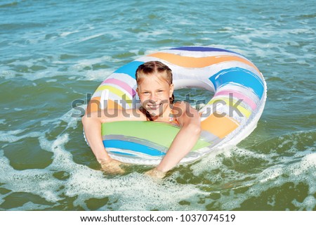 Happy child playing in blue water of ocean on a tropical resort at the sea.  Cheerful little girl swims in the blue ocean with an inflatable ring