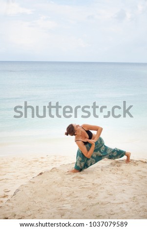 Beautiful woman doing virabhadrasana warrior yoga pose on the beach near the ocean