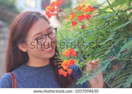 Asian tan skin wearing eyeglasses woman with long brown hair is smiling standing admiring the flowers