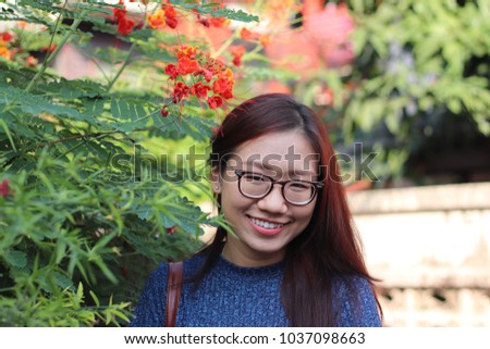 Asian tan skin wearing eyeglasses woman with long brown hair is smiling standing admiring the flowers