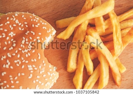 bitten Burger and French fries on a wooden Board.