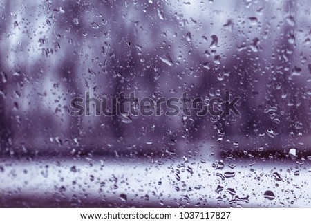 Raindrops on the windshield on a rainy winter day. Abstract beautiful romantic blurred landscape background through raindrops on the glass. Unusual abstract Background mood of romance