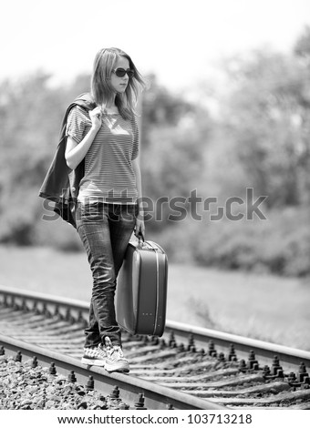 Young fashion girl with suitcase at railways. Photo in black and white style.
