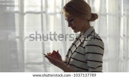 Young woman in a striped jacket with a phone on the window background.
