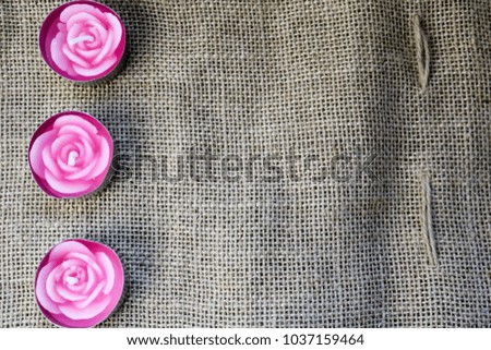 Three pink wax beautiful candles in the form of rose flowers with an unflavored wick against the background of an old brown linen cloth, linen hard, unbleached cloth made from vegetable fibers.