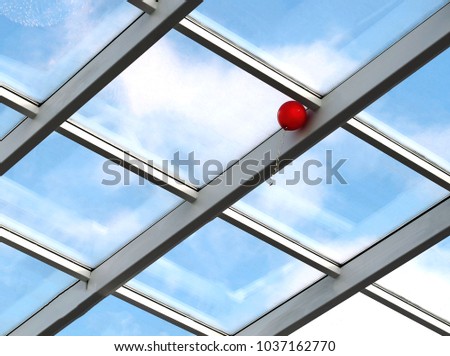 Background image. The roof of a building made of glass and metal against a blue sky. On a background of glass a red balloon. Can be used as a background or ad decoration wich copy space.