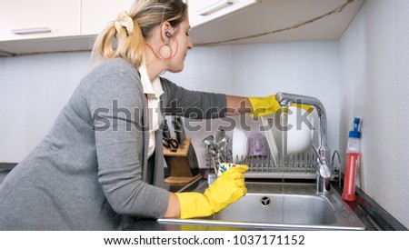 Portrait of housewife in yellow rubber gloves listening music and washing dishes