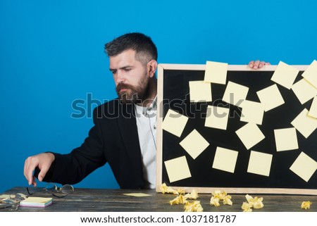 Notes. Business, planning, management, reminder. Bearded handsome businessman dressed in suit, sitting at table and holds board with stickers. People, employment, career and hiring concept.