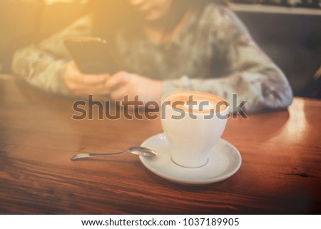 Girl texting on a date on her phone , top view image of coffee cup flat lay above the desk in a cafe with a spoon , in cafe or  home kitchen . Coffee latte drawing ,  Copy space , teens  social media