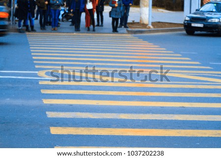 People waiting to cross the road by yellow pedestrian zebra. 