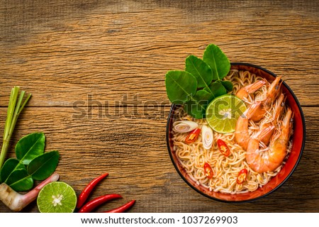 Thai style noodle in bowl, Tom Yum Kung with Thai herbs, chili, galangal, lime, lemongrass and kaffir lime leaf on wooden background. Royalty-Free Stock Photo #1037269903