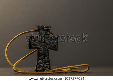 Distressed black wooden cross with leather strap on blurred grey background