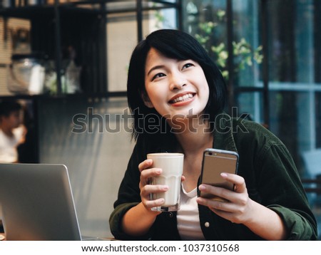 Young Asian woman drinking coffee and using laptop in coffee shop.