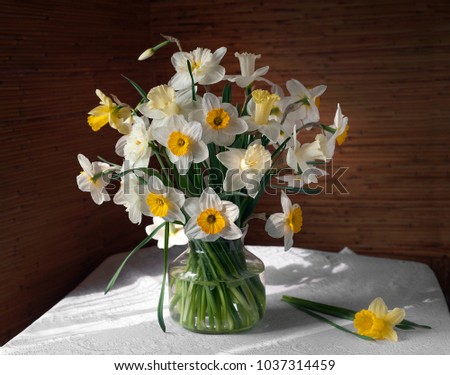 Still life with a bouquet of daffodils in glass vase on a table with a white tablecloth.