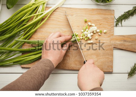 Woman cutting spring onion on wooden board for salad. Preparing organic food, natural homemade eating, top view, copy space