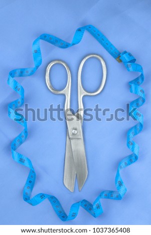 sewing tool: steel shiny big scissors and tape on blue fabric