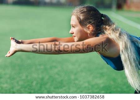 sports girl in a blue shirt and leggings doing gymnastics workout on a football field. Fitness, sport, health energy. Close up